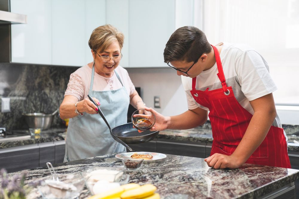 Caregiver helping a senior woman prepare food in her home kitchen