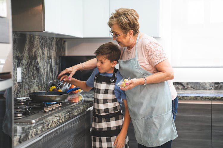 Boy And Elderly Woman Wearing Aprons Cooking 