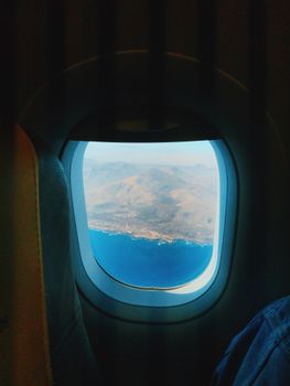 A breathtaking view of blue ocean and mountains from an airplane window.