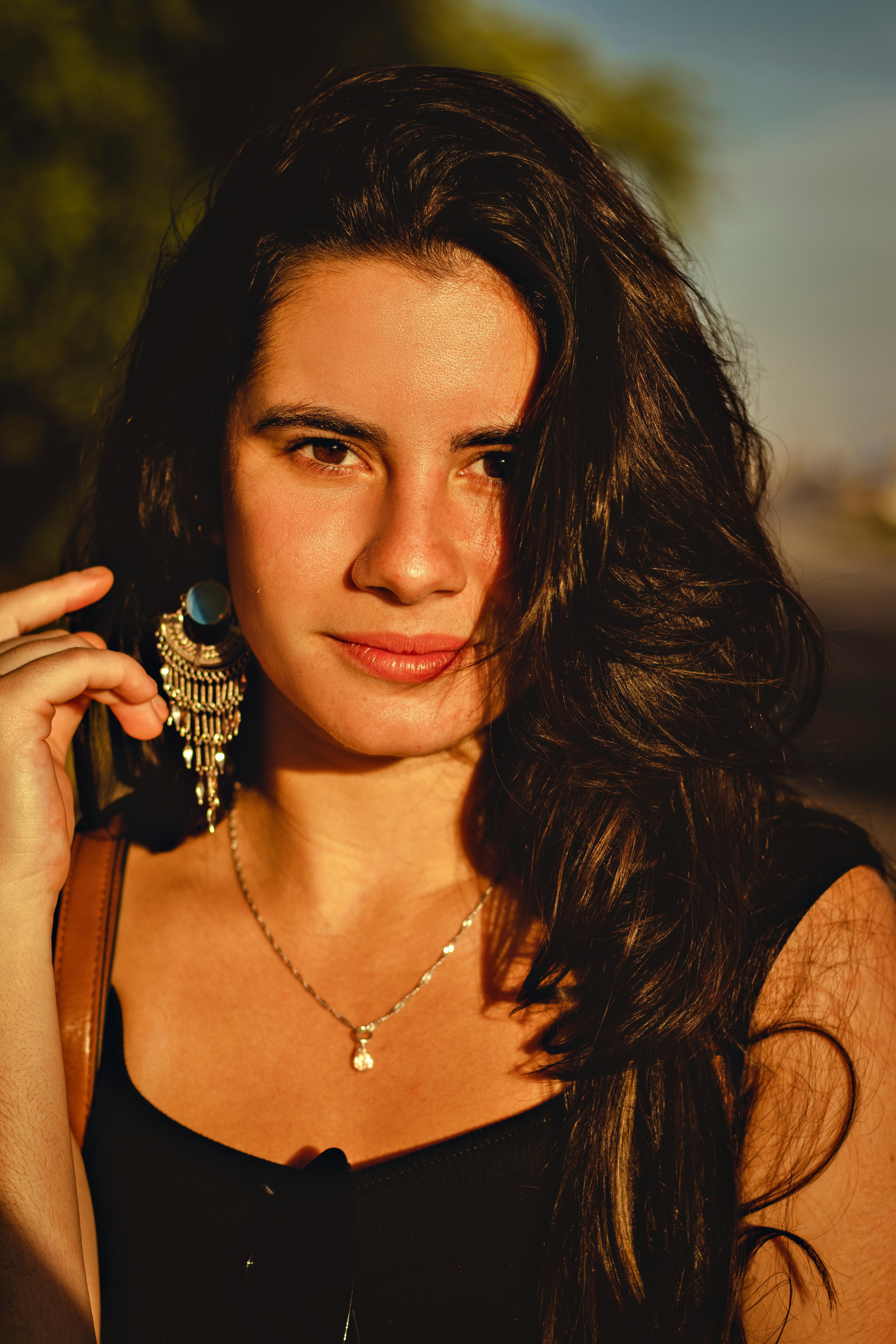 Portrait of a woman wearing statement earrings and necklace, captured in warm natural light.