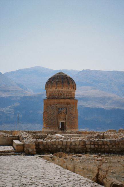 A historical stone temple set against a mountainous landscape under a clear sky.