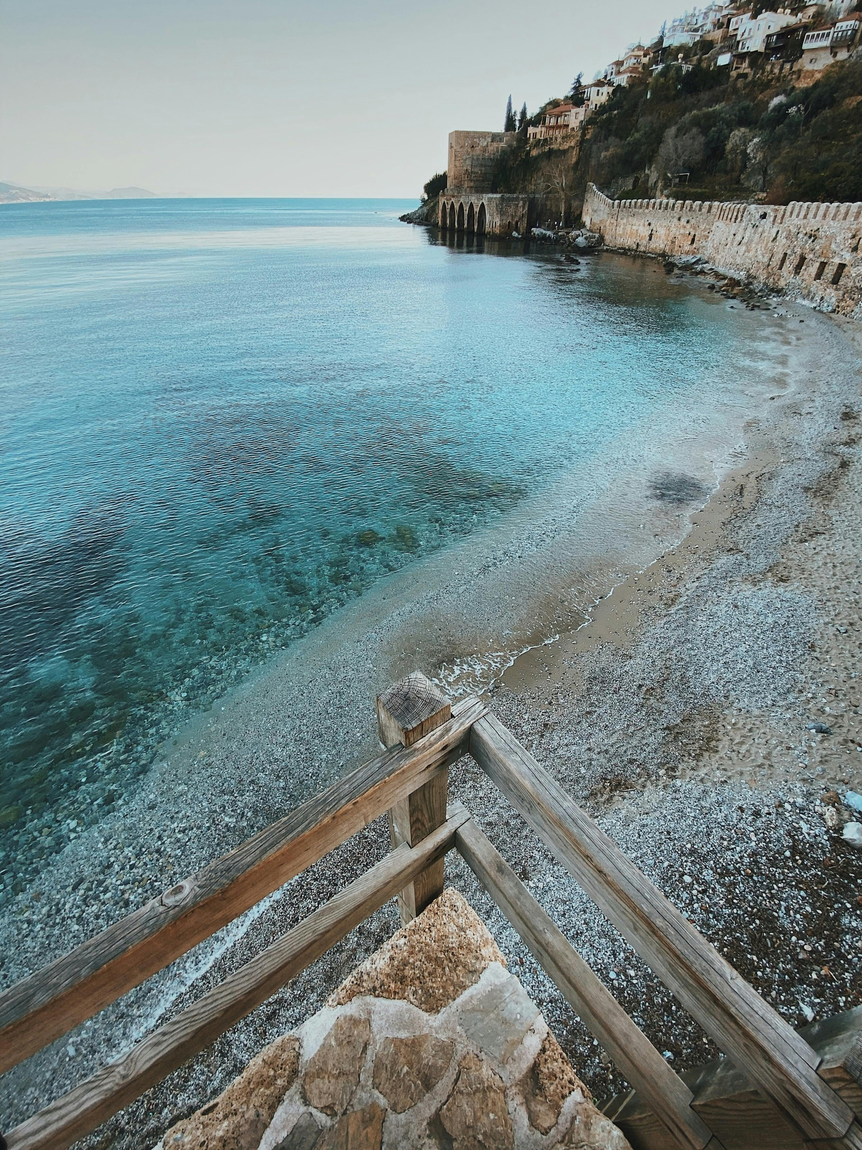 Tranquil shoreline of Alanya with clear turquoise waters and ancient fortress walls, offering a serene coastal retreat.