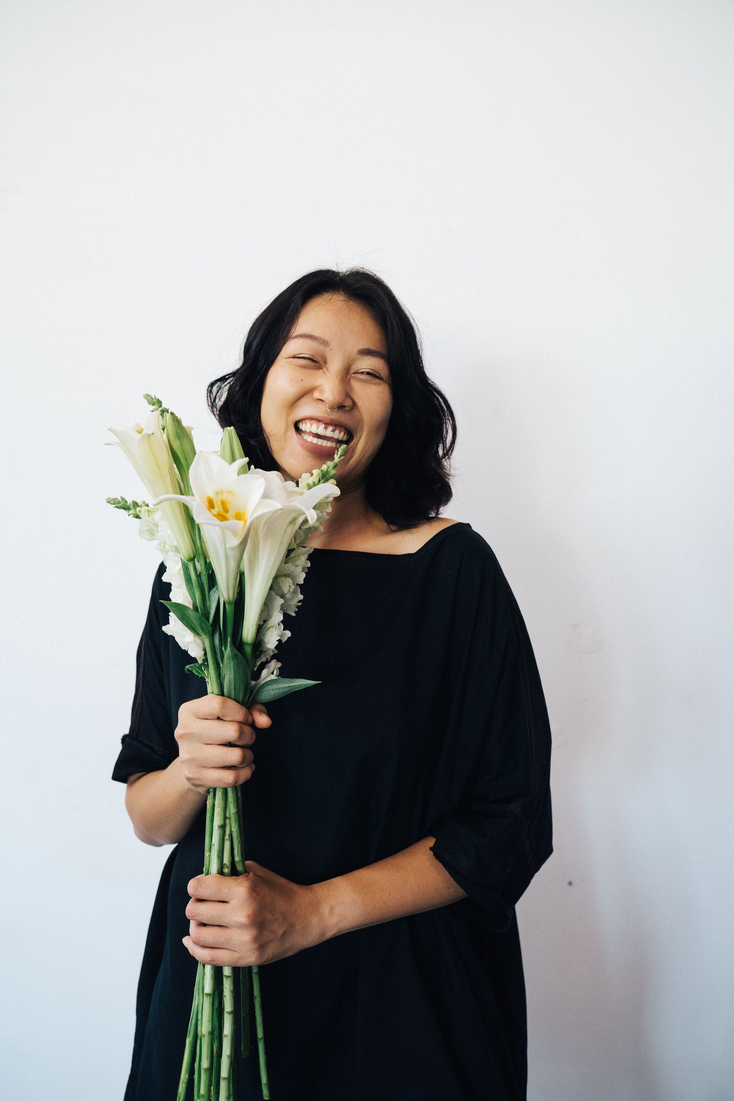 Portrait of a happy woman in a black dress holding white lilies with a joyful smile.
