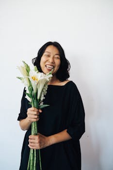 Portrait of a happy woman in a black dress holding white lilies with a joyful smile.