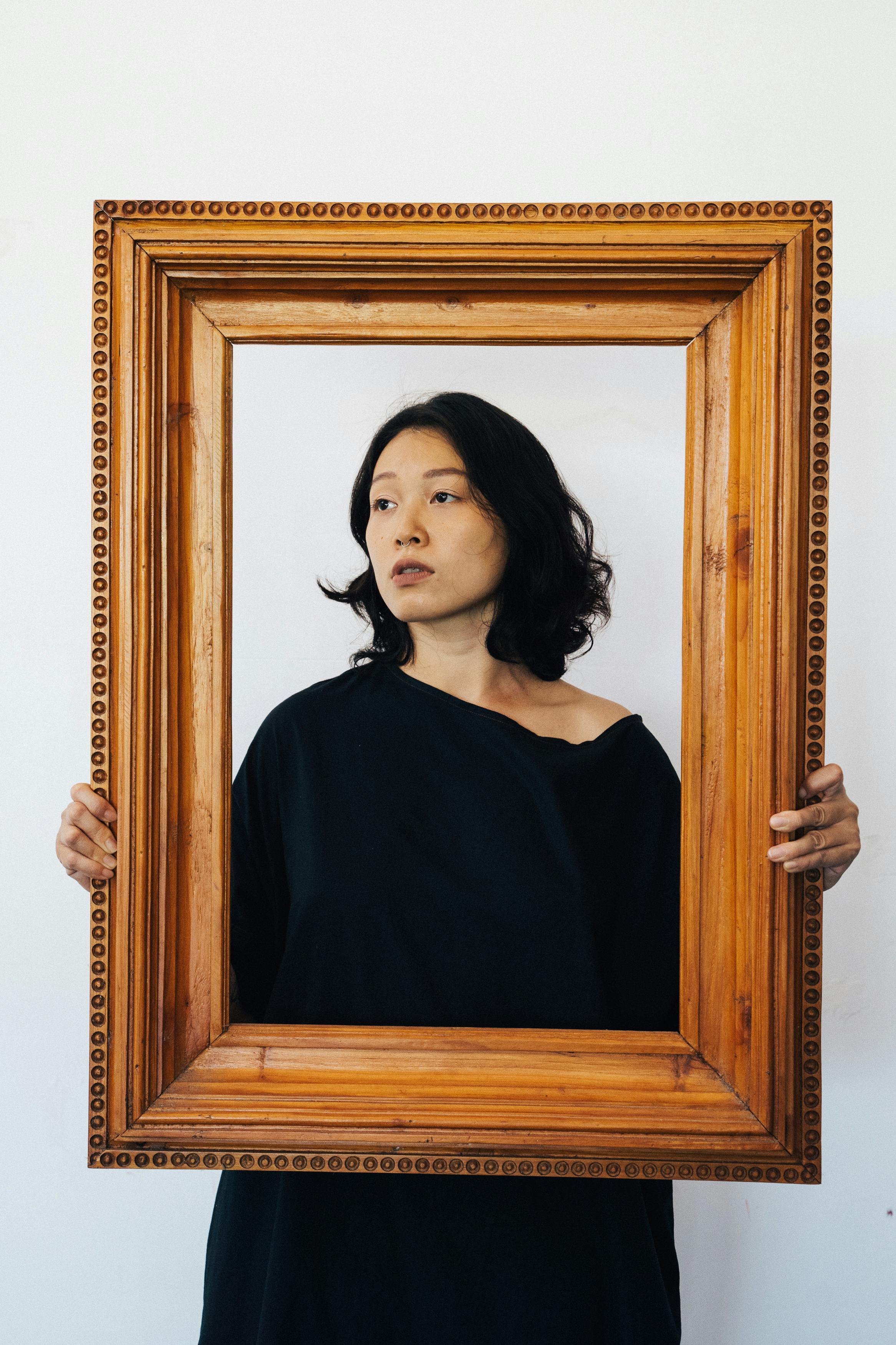 A stylish portrait of an Asian woman posing with a wooden frame against a white background.