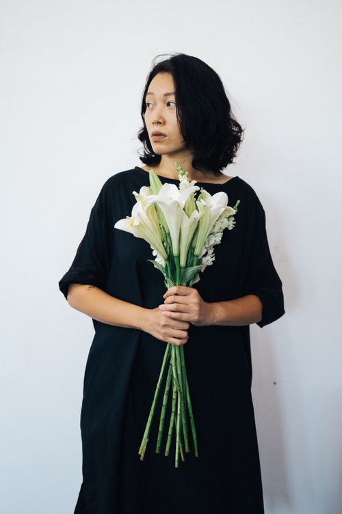 Free Portrait of an Asian woman in a black dress holding a bouquet of white lilies against a plain background. Stock Photo
