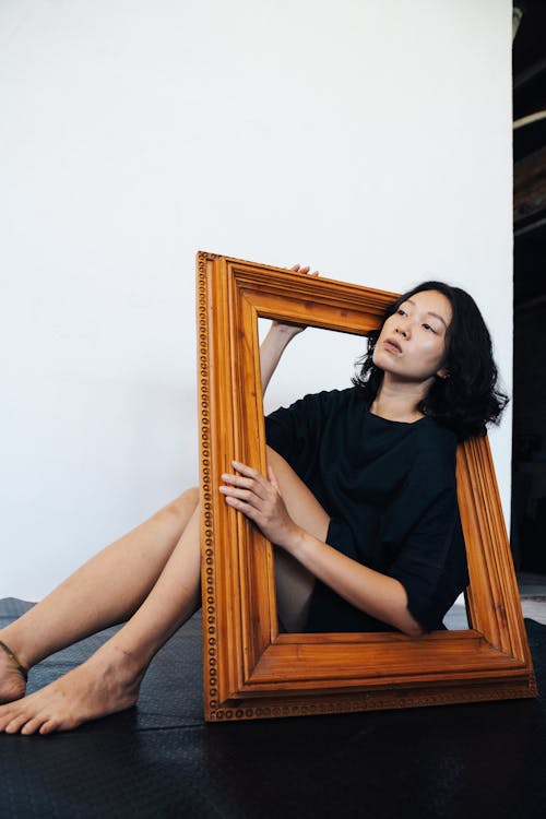 Woman in Black Dress Sitting on Brown Wooden Frame