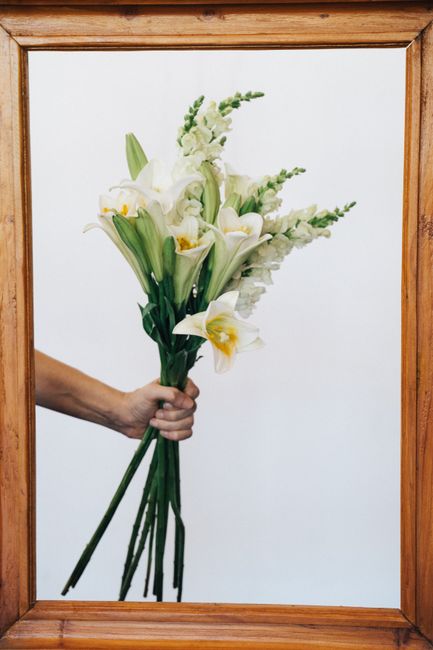 A hand holding a bouquet of white lilies elegantly framed against a plain background.
