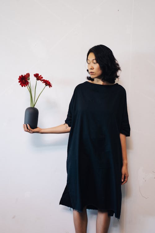 Woman in Black Dress Holding a Black Vase with Red Flowers · Free