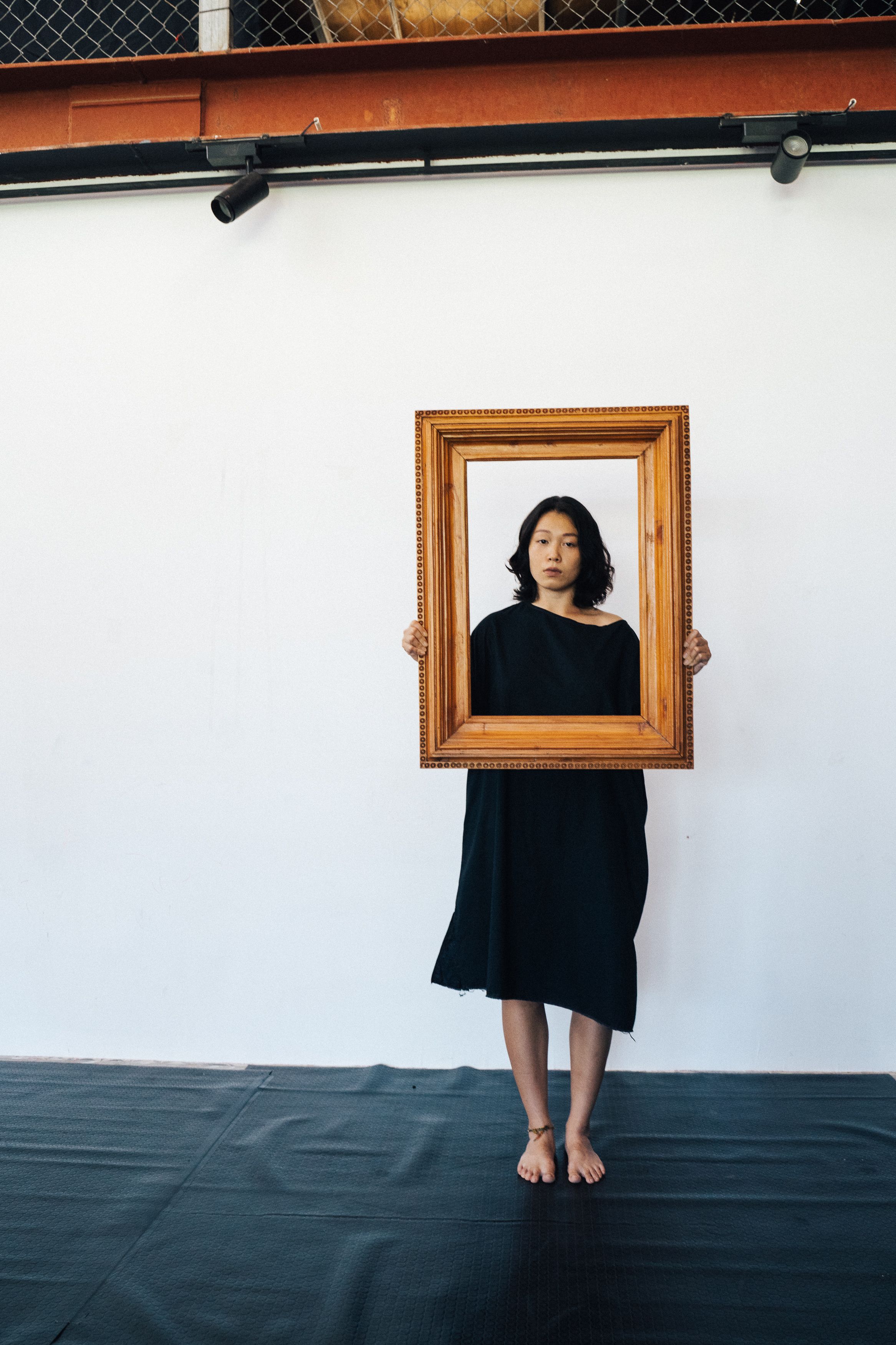 Asian woman posing with wooden frame on white background, studio setting.