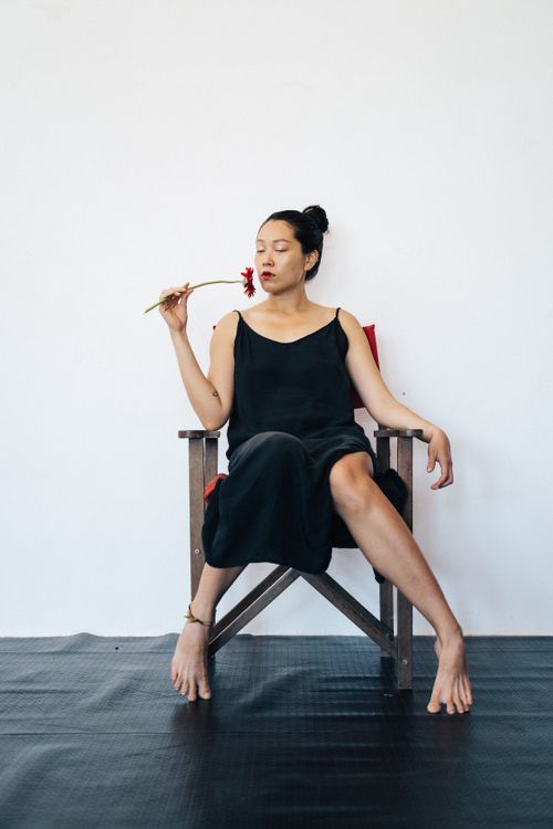 Free Minimalist portrait of a woman in black dress holding a red flower, sitting on a chair. Stock Photo