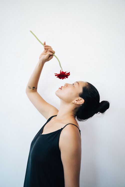 Free An elegant woman in a black tank top holding a red flower against a minimalist white background. Stock Photo