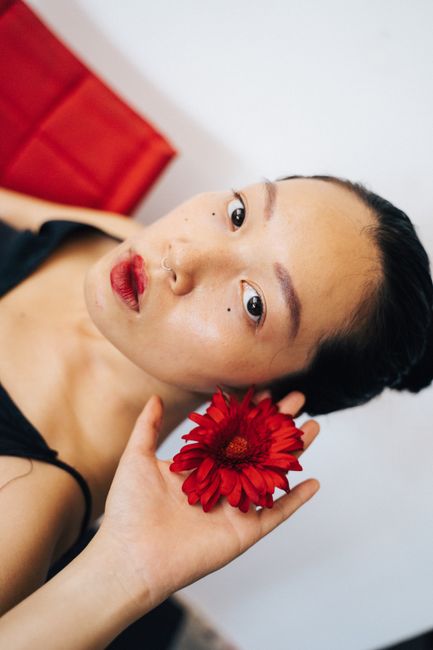 A woman holds a vibrant red flower near her face, creating a striking and elegant portrait.