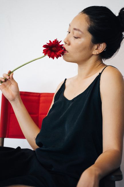 Woman in black dress posing with red flower indoors.