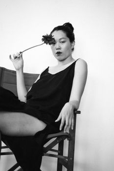 Artistic black and white portrait of a woman holding a flower and sitting on a folding chair.