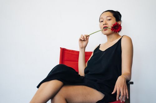 Free A woman in a black dress poses with a red flower in a stylish studio setting, showcasing sensuality. Stock Photo