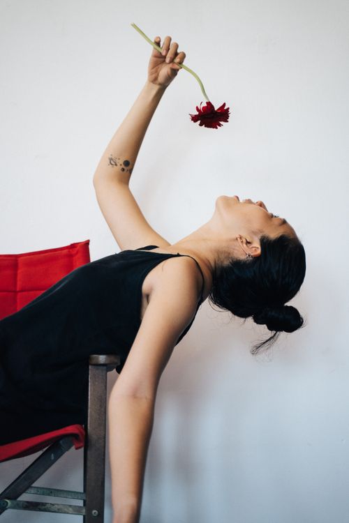 Free Artistic photo of a woman reclining on a chair holding a red flower against a white background. Stock Photo