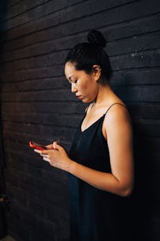 Profile of woman with hair bun using smartphone indoors against dark wall.