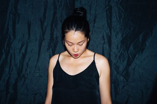 Free Studio portrait of a woman in a dark dress looking down against a black backdrop. Stock Photo