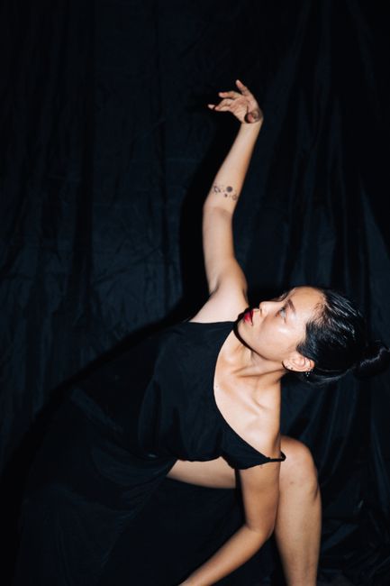 Asian woman in elegant black dress striking a dramatic dance pose.