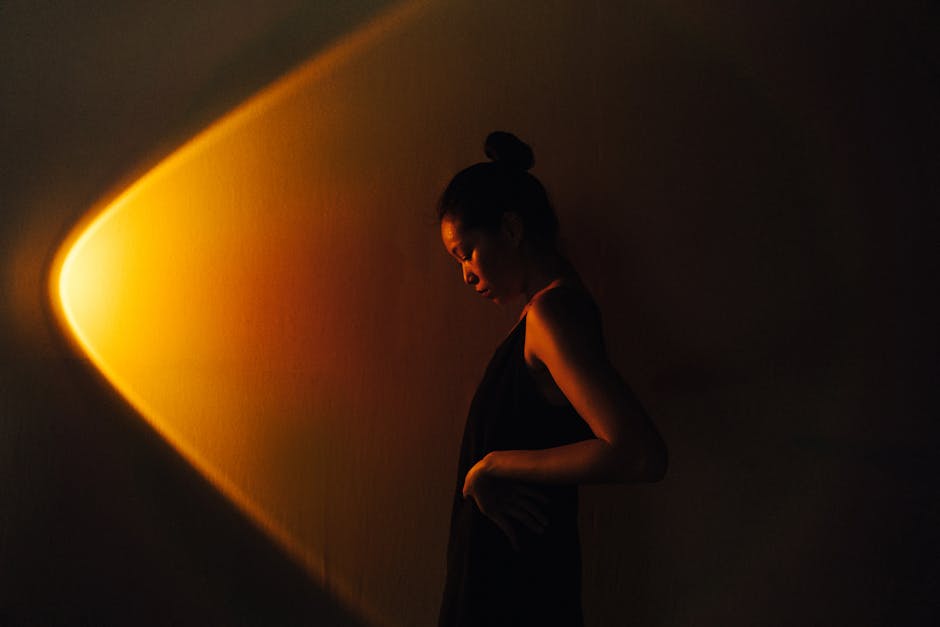 Side profile of an Asian woman in a dark studio setting with dramatic lighting.