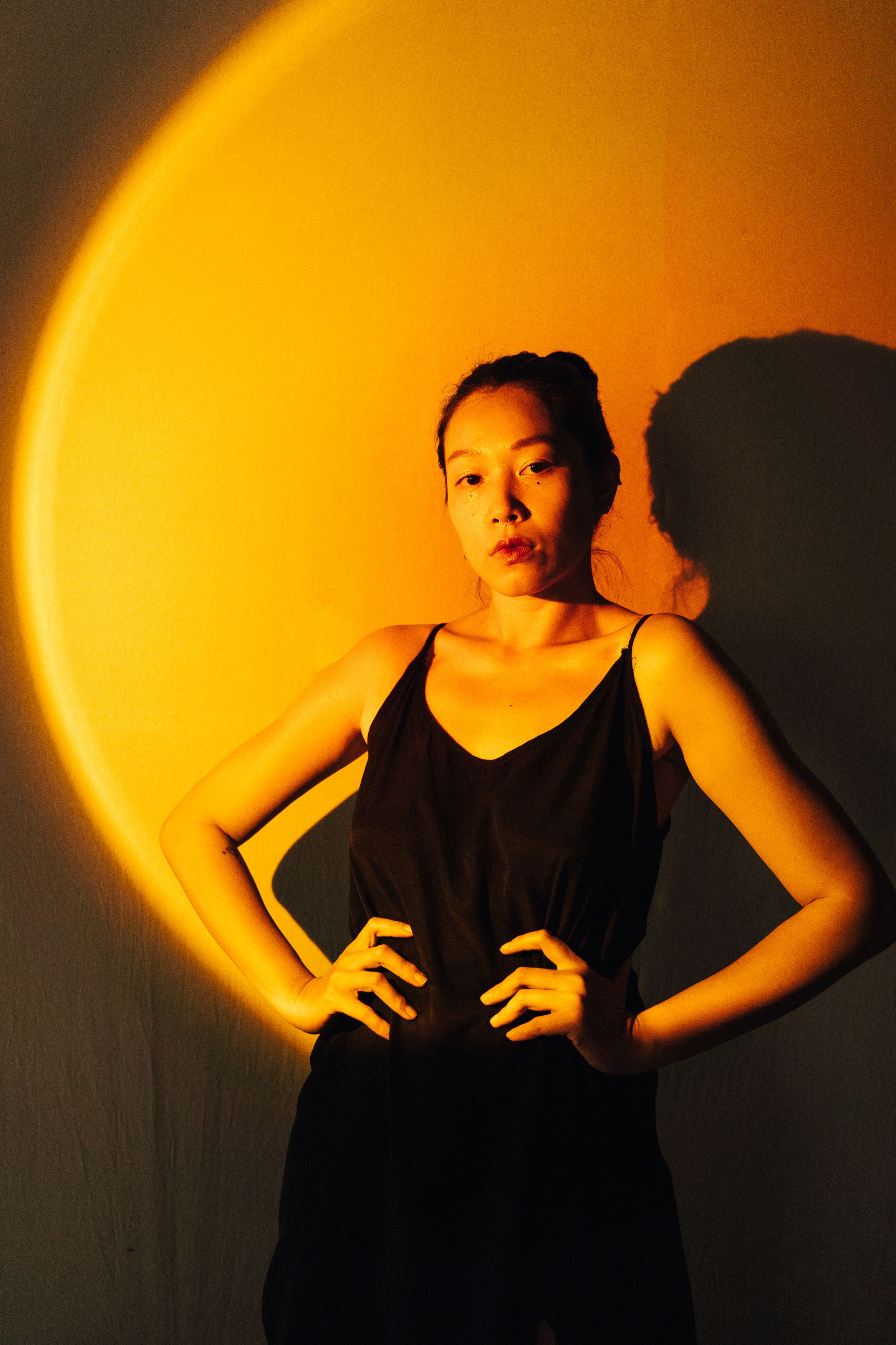 Fashion portrait of a woman posing under dramatic lighting with hands on her waist.