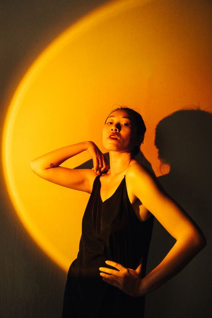 Fashionable Asian woman poses in dramatic lighting, showcasing modern style and elegance.