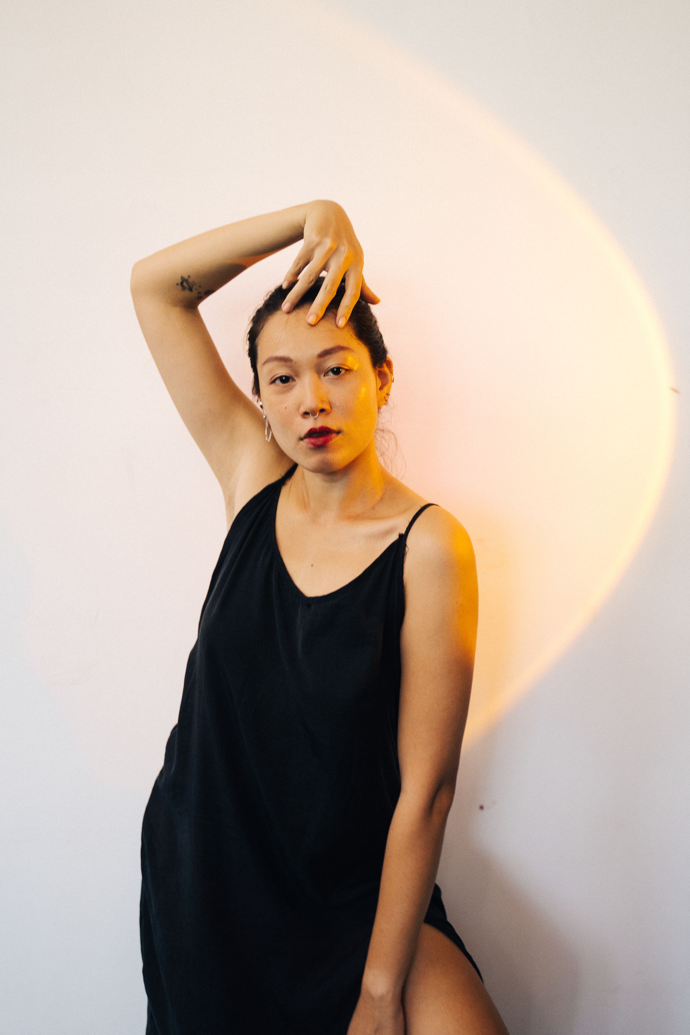 A fashionable Asian woman in a black dress poses with dramatic lighting to create a modern, glamorous look.