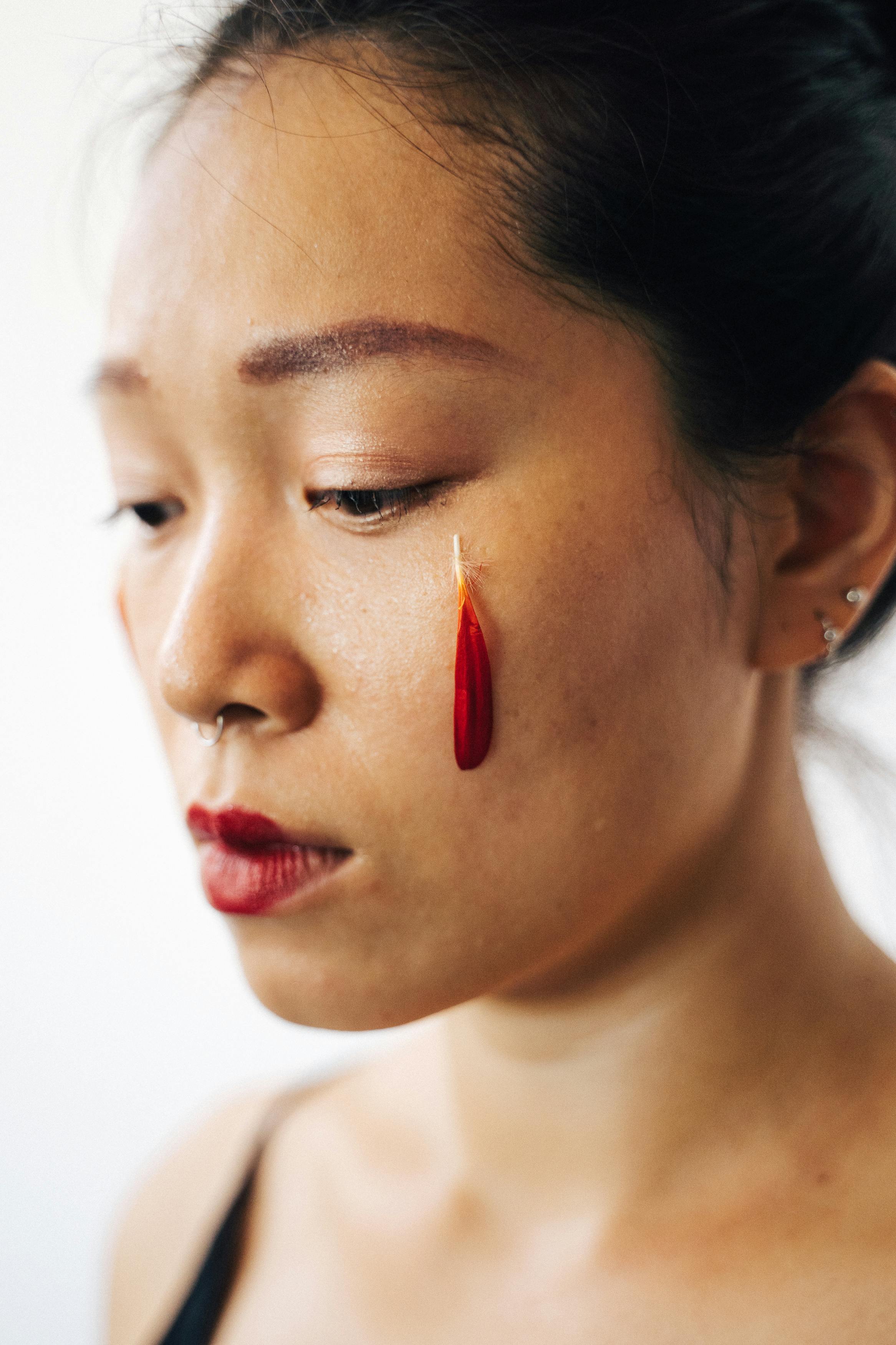 Close-up of a woman with expressive makeup featuring a red feather and nose ring.