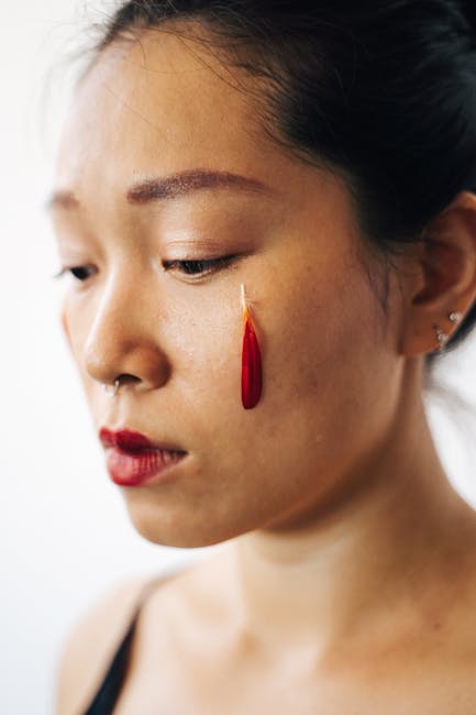 Close-up of a woman with expressive makeup featuring a red feather and nose ring.