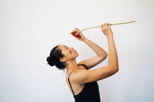 Free Side view of an elegant woman holding a red flower against a white background. Stock Photo