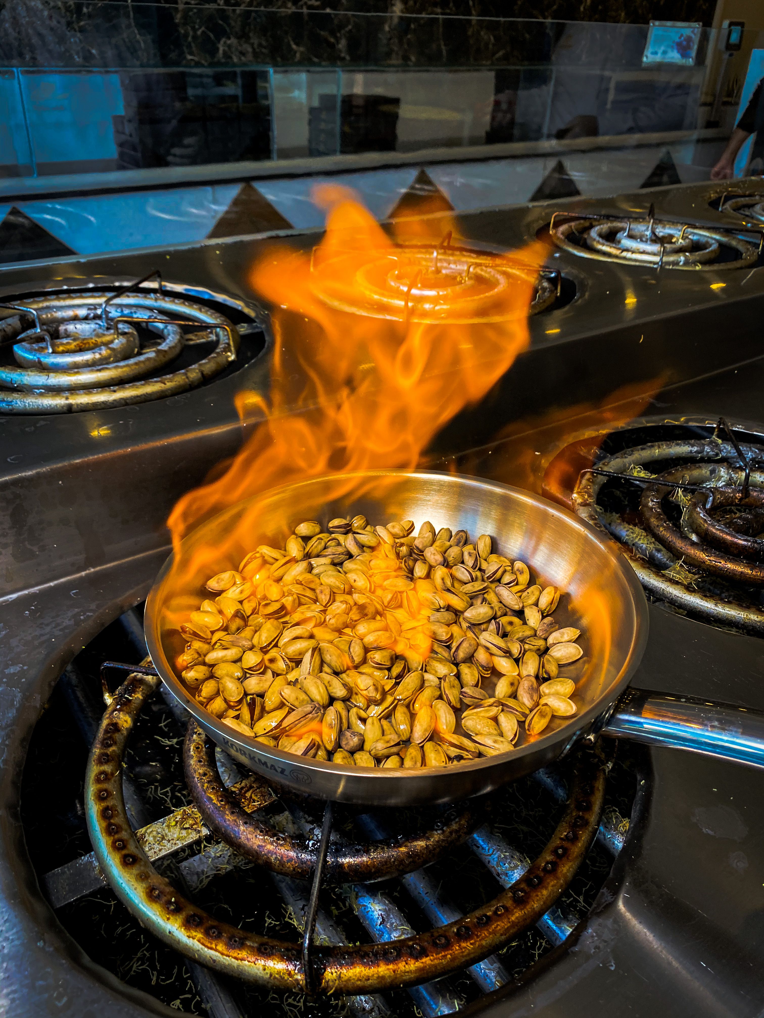 Pistachios roasting in a pan over a stove with visible flames, captured indoors.