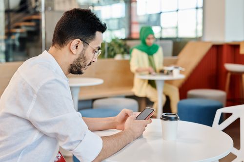 Free Man in a cafe using a smartphone, drinking coffee, depicting modern lifestyle. Stock Photo