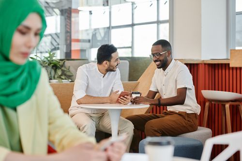 Free Two friends engage in lively conversation while enjoying coffee in a modern cafe setting. Stock Photo