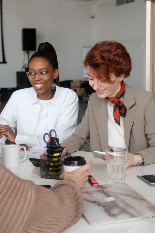 Free Two women collaborating in an office setting, smiling and engaged, with various office supplies and a laptop. Stock Photo