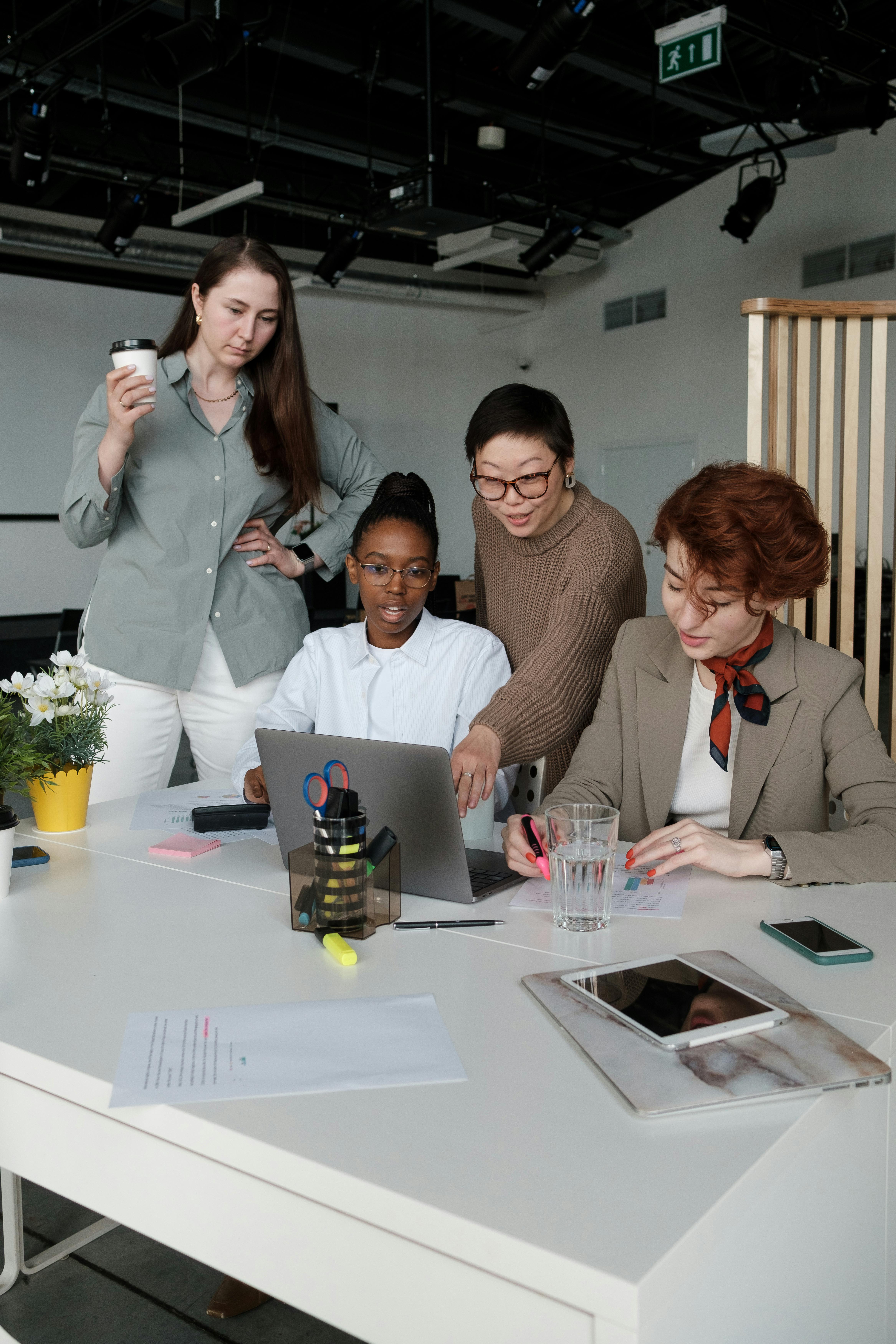 A diverse group of women collaborating in a modern office setting with technology and documents.