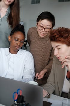 A diverse group of colleagues collaborating around a laptop in a modern office setting.