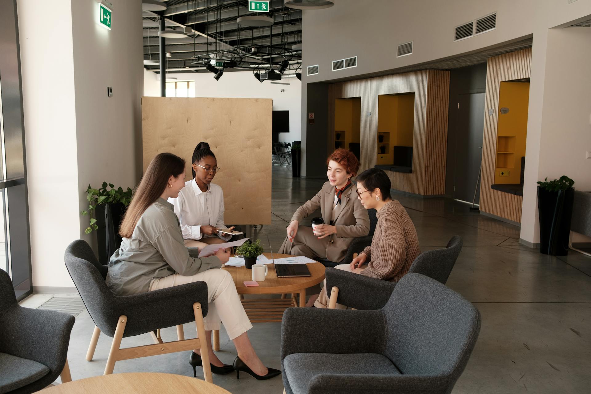 Group of professionals collaborating in a modern office lounge area, engaging in team discussions.