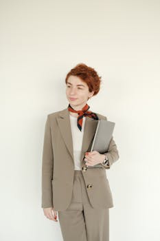 Stylish young woman in a suit with a scarf holding a laptop, embodying professionalism.