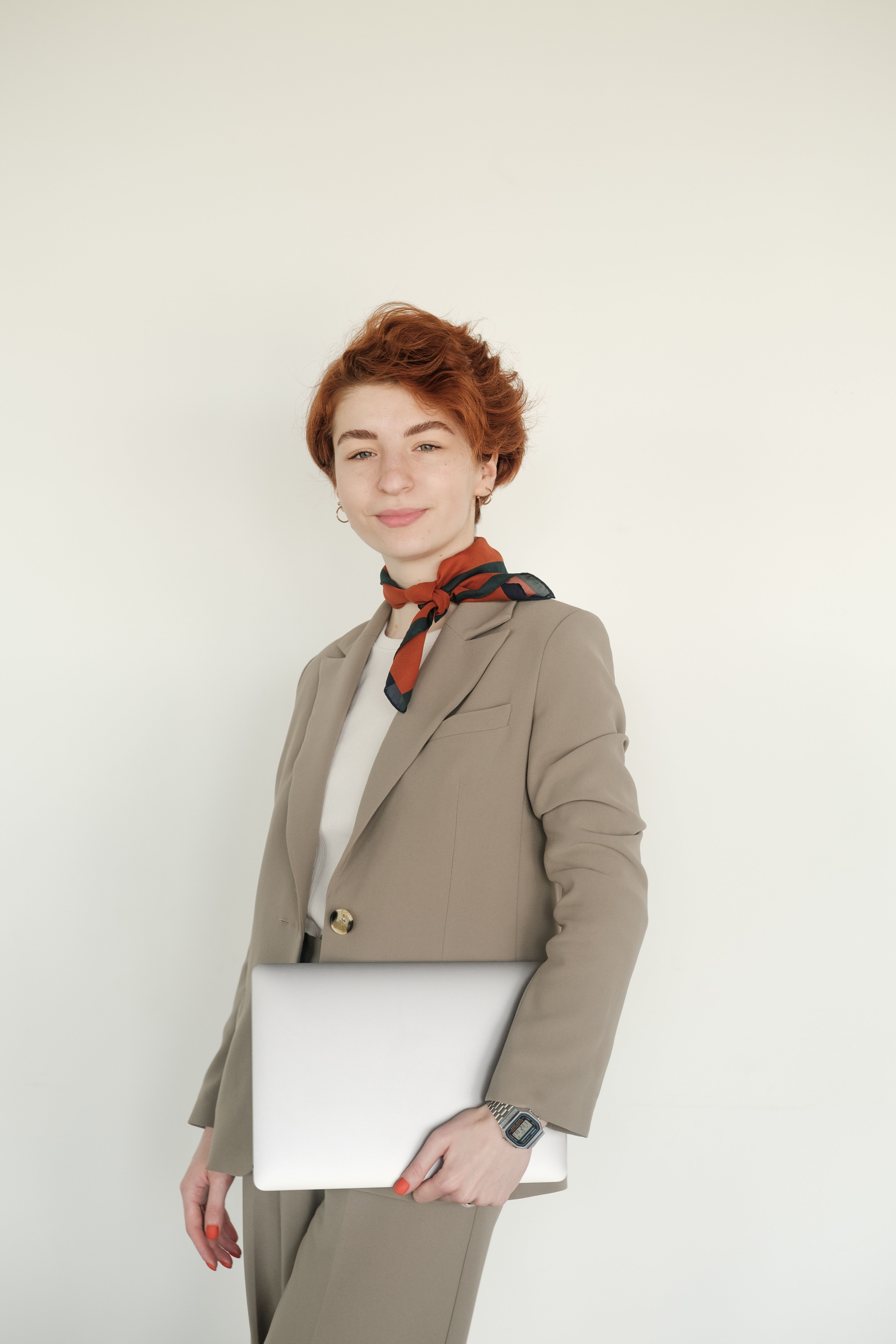 Confident woman in a suit holding a laptop, wearing a stylish neckerchief.