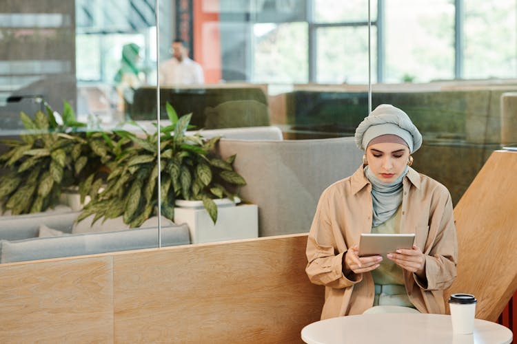 Woman With Headscarf Using An IPad Inside A Coffee Shop 