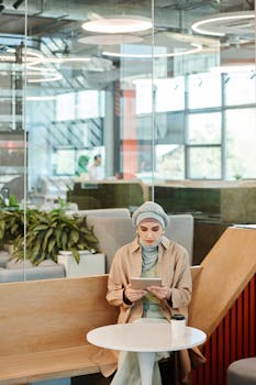 A woman in a stylish coffee shop reading on a tablet, surrounded by modern decor and natural light.