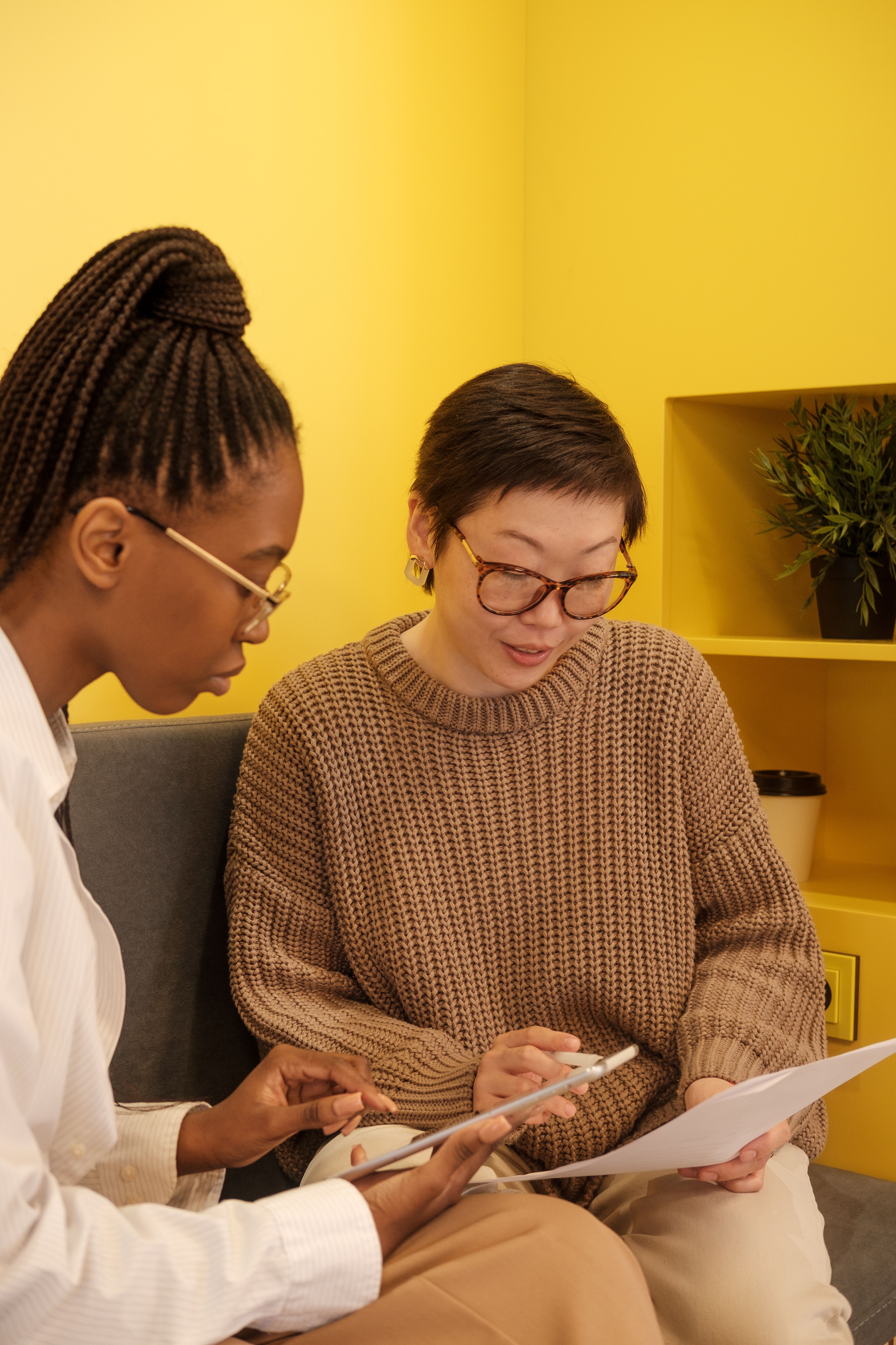 Mobile Application Development - Two businesswomen discuss strategies using tablets in a modern office setting.