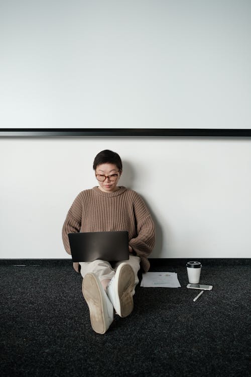Woman Sitting on the Floor Using Laptop in a Conference Room 