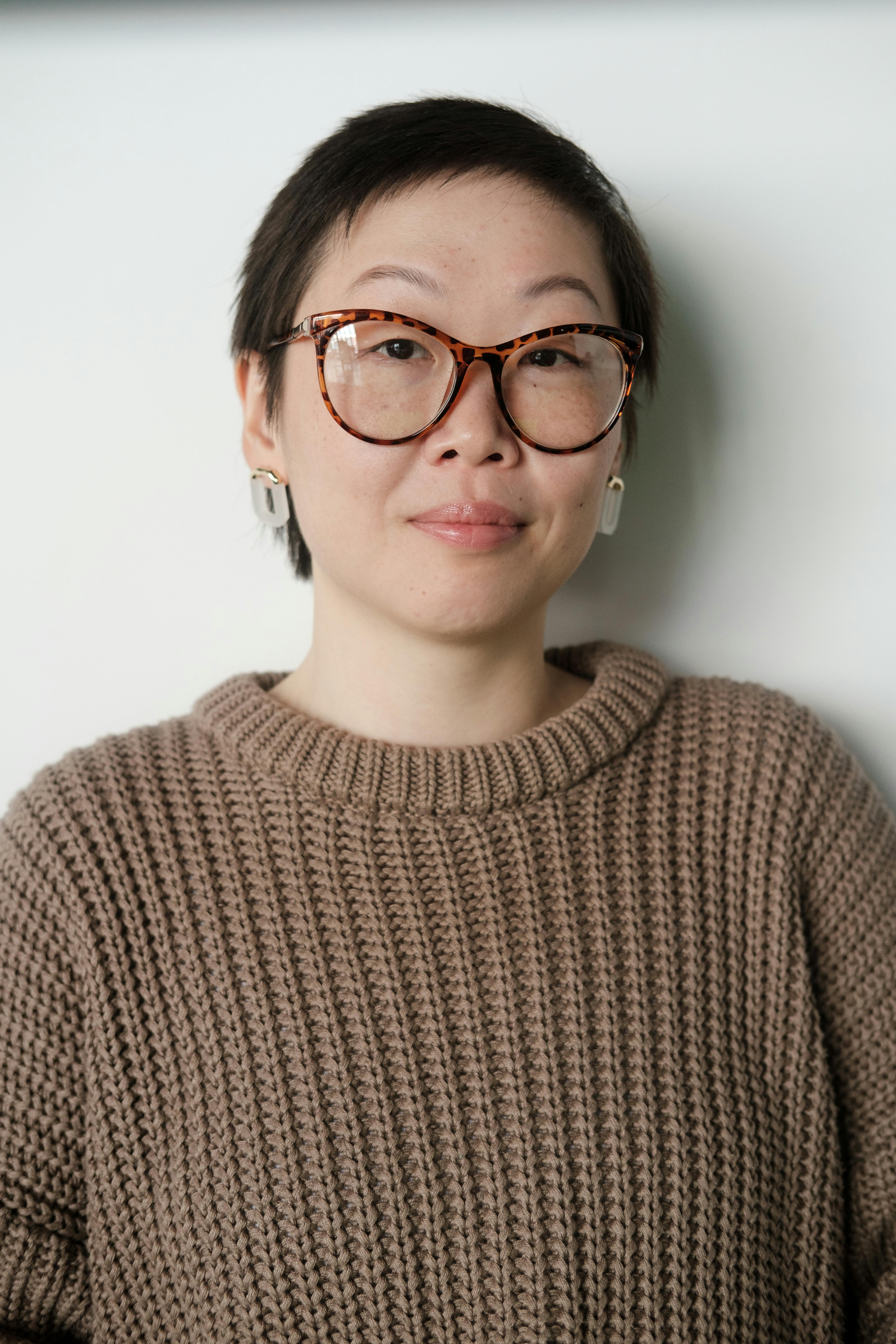Portrait of a fashionable woman wearing glasses and a cozy sweater in a studio setting.