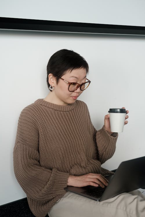 A Woman Working While Holding a Coffee Cup 