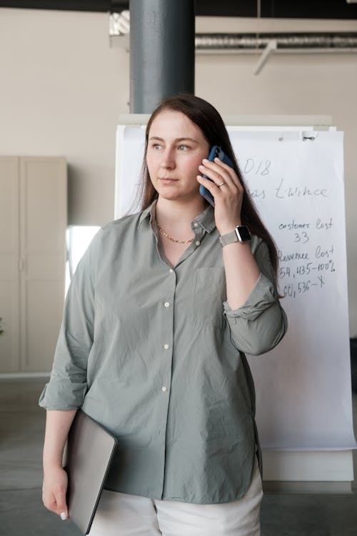 Woman Holding a Laptop While on a Phone Call