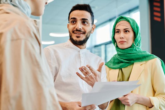 Two professionals in conversation during an office meeting, holding documents and collaborating with a colleague.