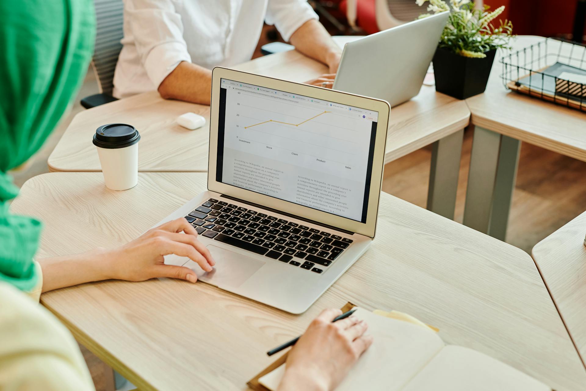 A modern workspace with people using laptops, focusing on data analysis on screen.