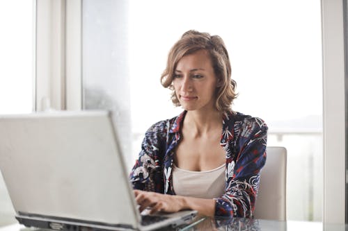 gratis Vrouw In Blauwe Bloemen Top Zitten Tijdens Het Gebruik Van Laptop Stockfoto